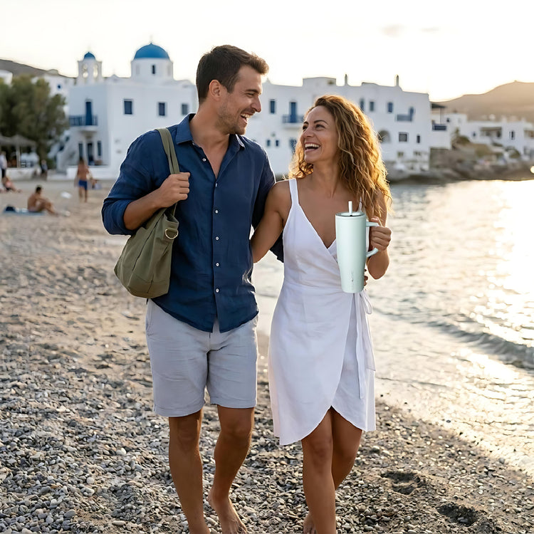 coolnmore Aqualis vogue tumbler θερμος 1200ml με καλαμακι ανοξειδωτο. Couple at the beach holding a blue tumbler with scenic background