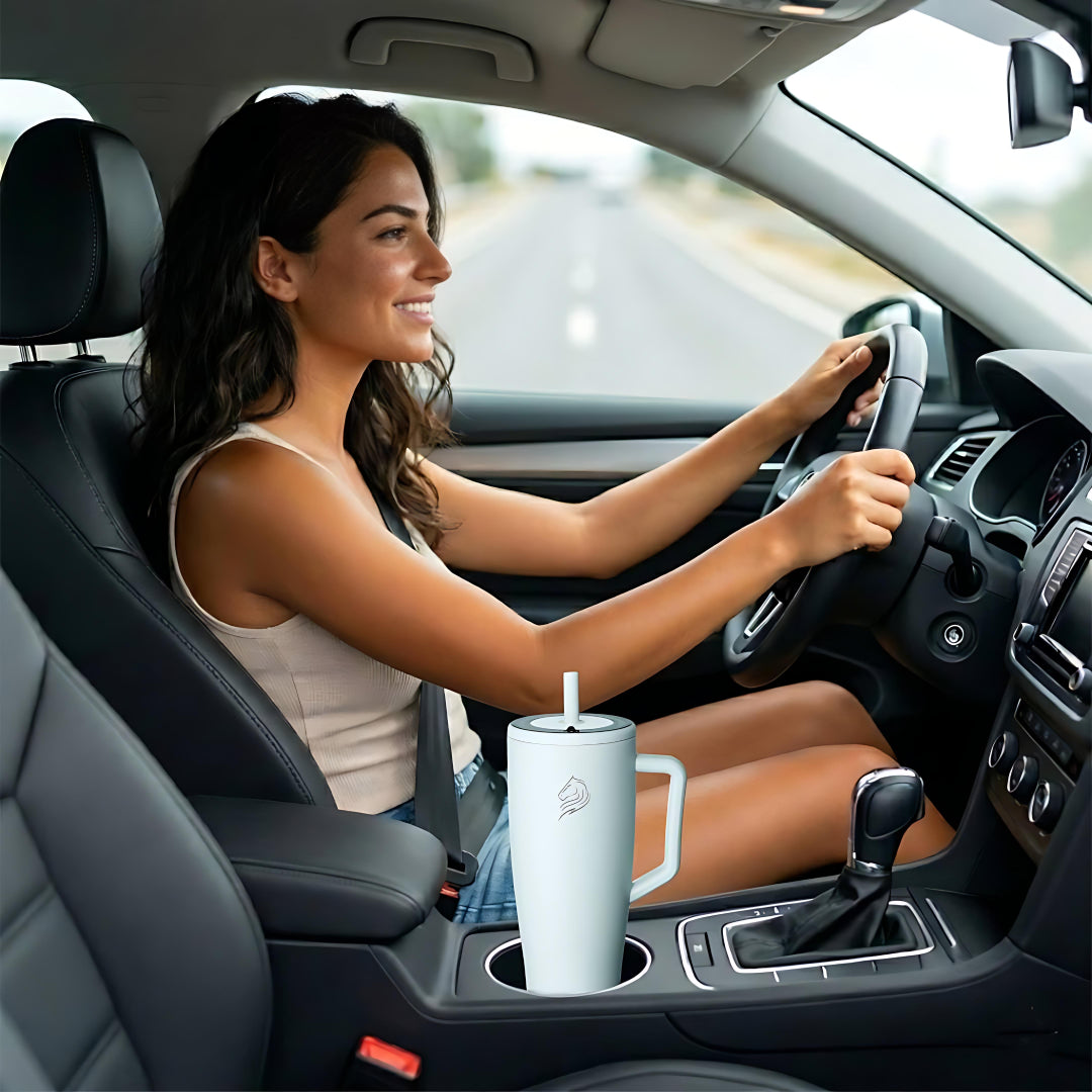 Woman driving a car with a light blue tumbler in the cup holder. coolnmore Aqualis vogue tumbler θερμος 1200ml με καλαμακι ανοξειδωτο