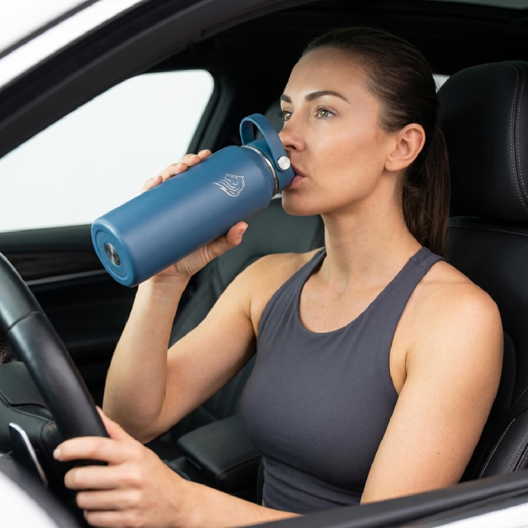 Coolnmore Denim θερμος νερου 1 λιτρου με καλαμακι. Woman drinking from a blue water bottle inside a car