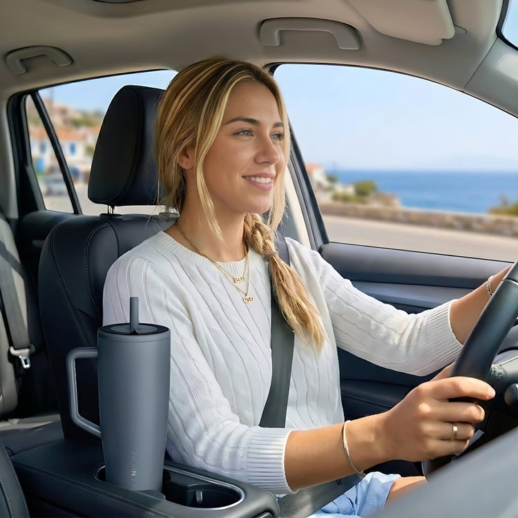 Woman driving a car with a grey tumbler in the cup holder. coolnmore titanium vogue tumbler θερμος 1200ml με καλαμακι ανοξειδωτο