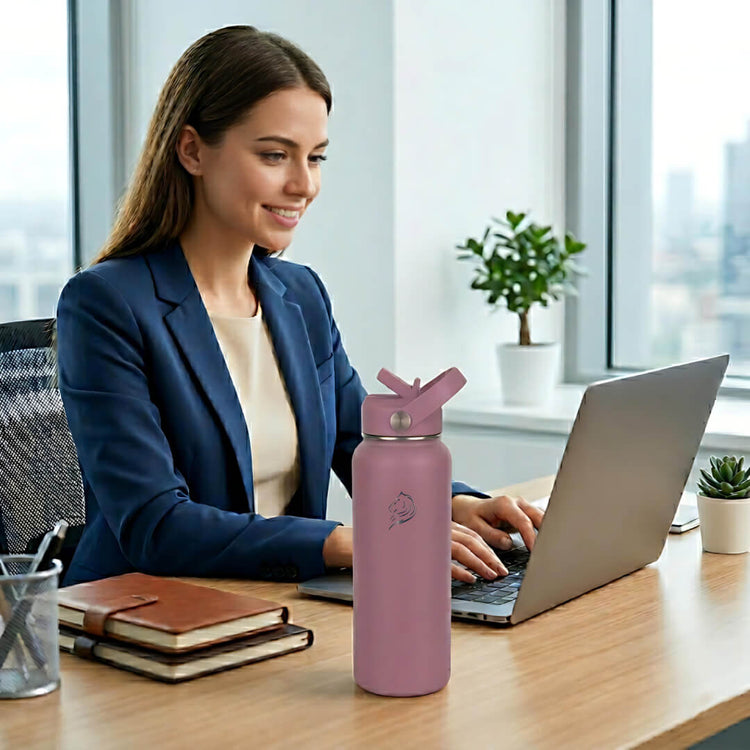 Woman working on a laptop with a purple water bottle on a desk in an office setting, Coolnmore θερμος νερου 1 λιτρου με καλαμακι. 