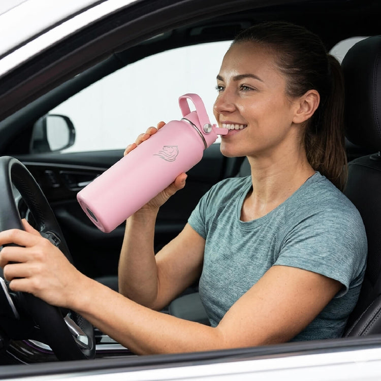Coοlnmore Flamingo θερμος νερου 1 λιτρου. Γυναικα χαρουμενη οδηγωντας πινει νερο απο το μπουκαλι θερμος της