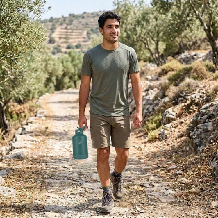 coolnmore moss green μπουκαλι θερμος 1.5 λιτρο.  Man walking on a trail holding a green water bottle, surrounded by greenery.