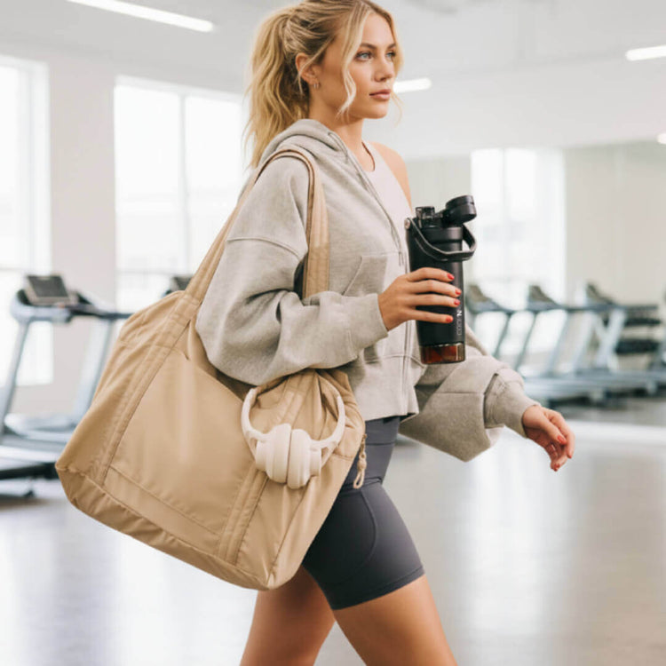Coolnmore shaker πρωτεινης θερμος 700ml. Woman in a gym holding a beige tote bag and a shaker bottle.